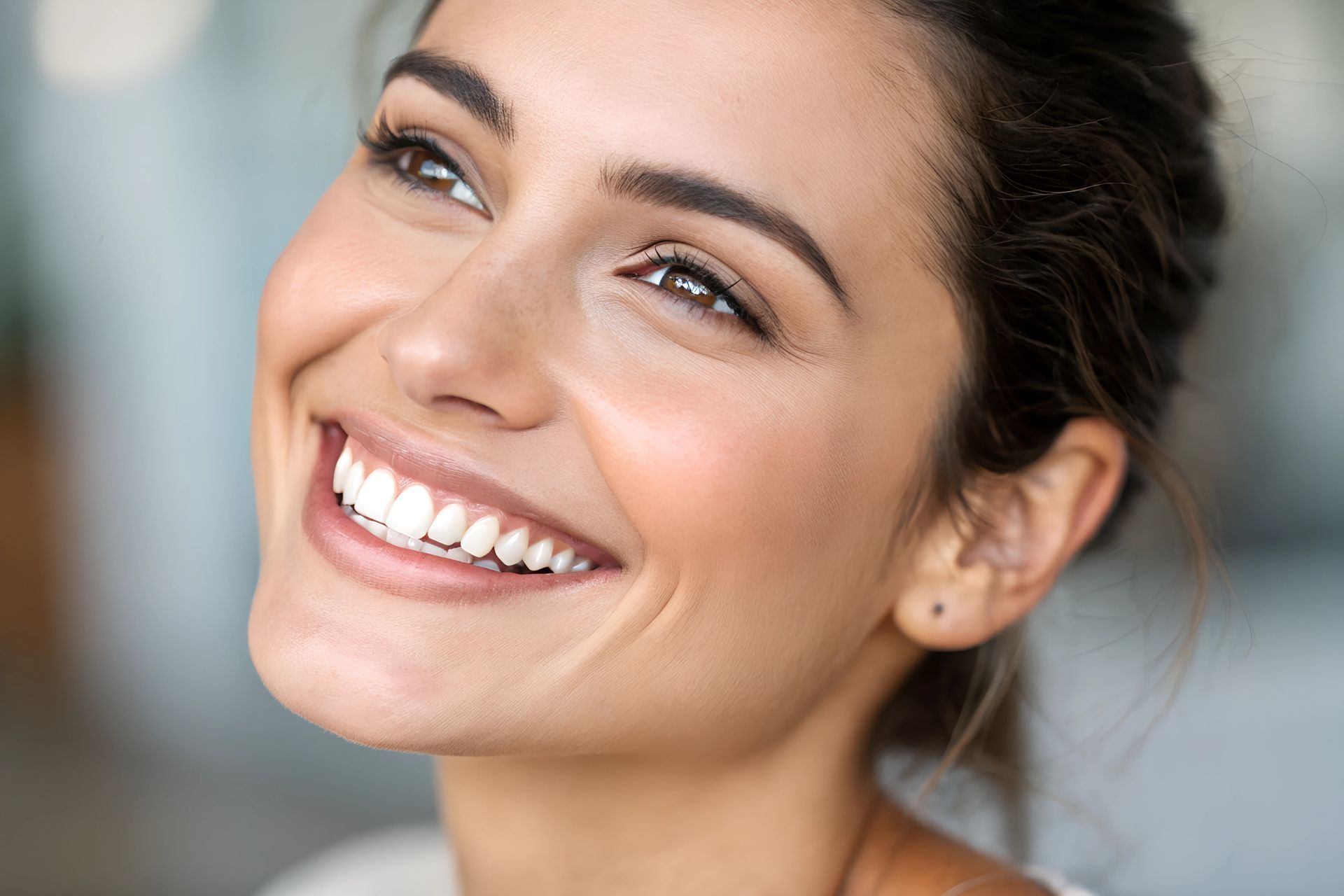 Une femme aux cheveux bruns arbore un large sourire, révélant ses dents blanches. Son visage est illuminé et elle regarde vers le haut.
