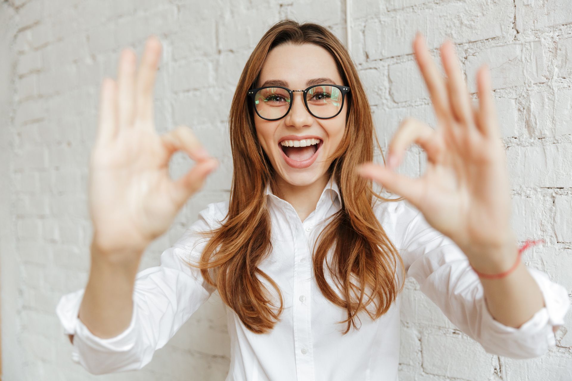 Une femme portant des lunettes fait un signe ok avec ses mains.