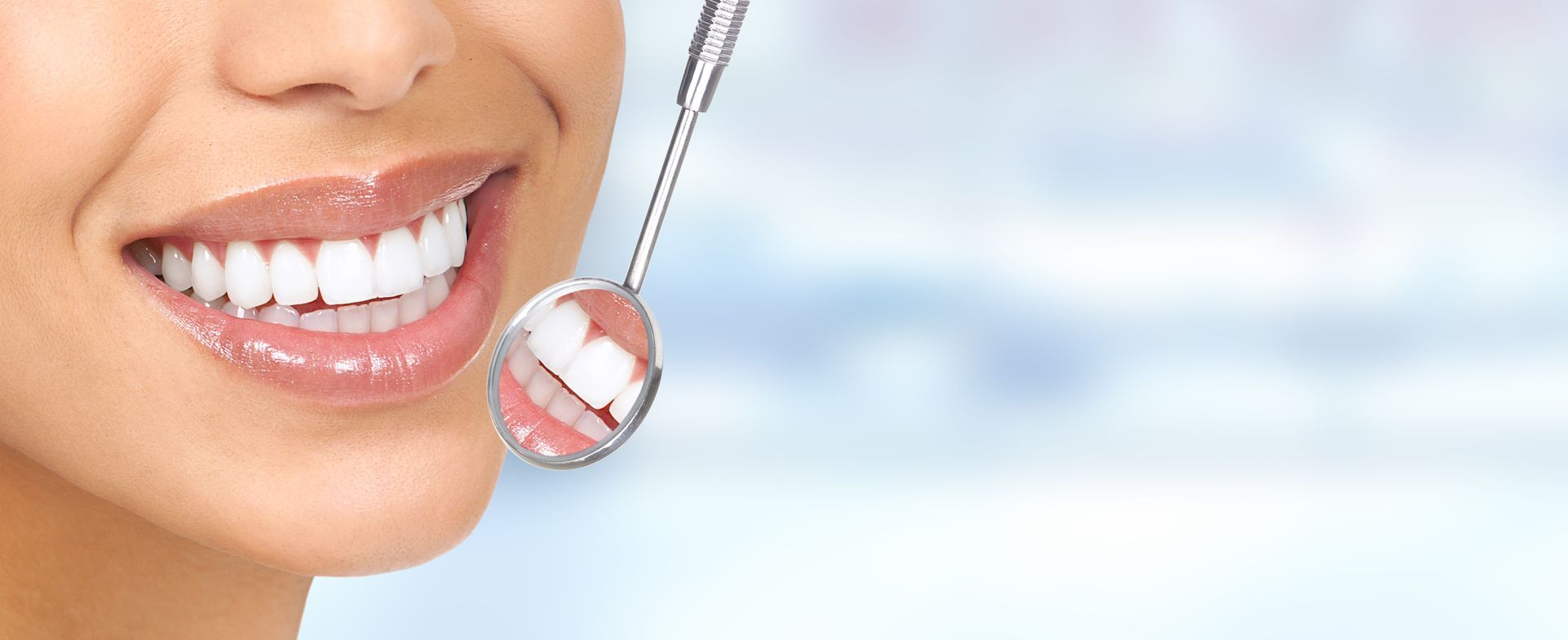 La bouche d'une personne souriante, avec des dents d'un blanc éclatant, examinée par un miroir dentaire sur un fond bleu flou.