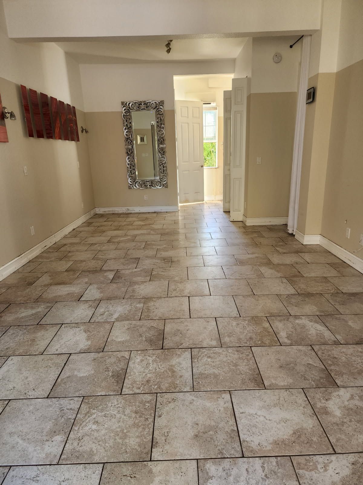 Empty room with tiled floor, beige walls, and a decorative mirror.