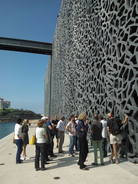 A group of people standing in front of the concrete facade of the museum MUCEM in Marseille.
