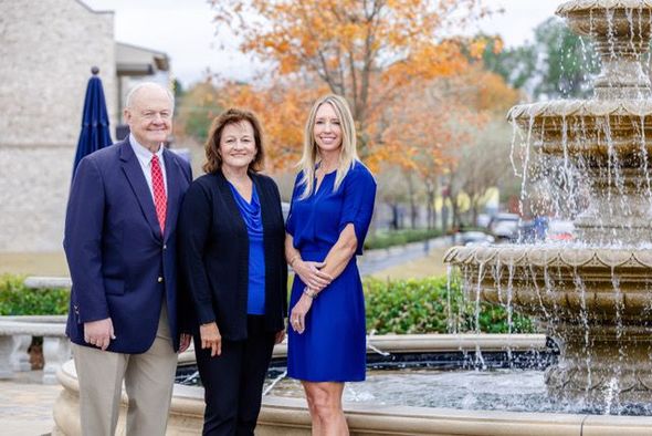 Three people standing in front of a building with a fountain, smiling and posing for a formal portrait.