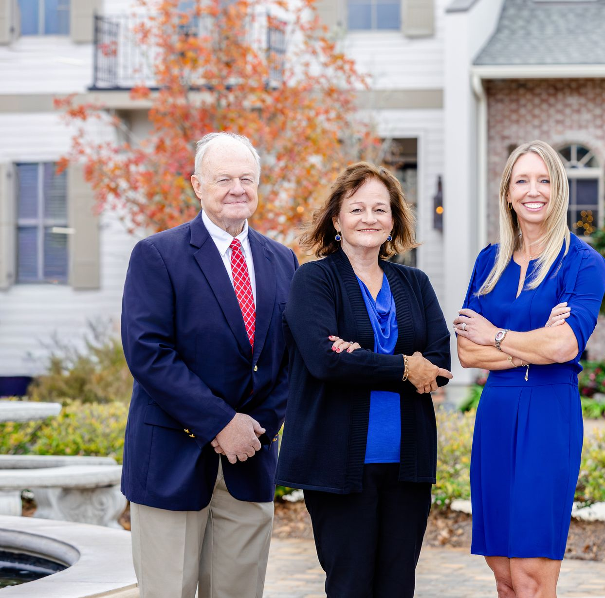 Three people standing in front of a building with a fountain, smiling and posing for a formal portrait.