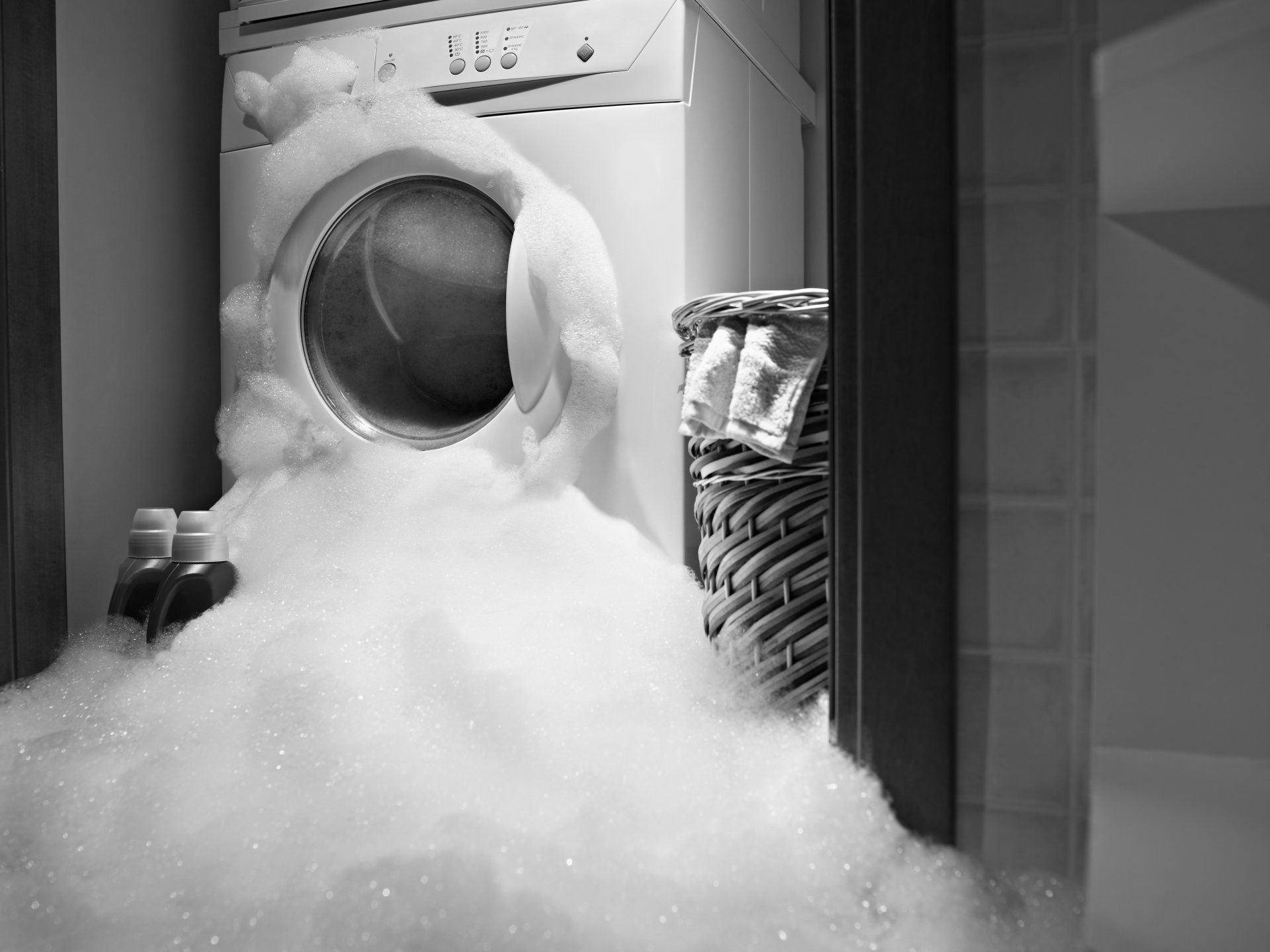 a washing machine is covered in foam in a laundry room .