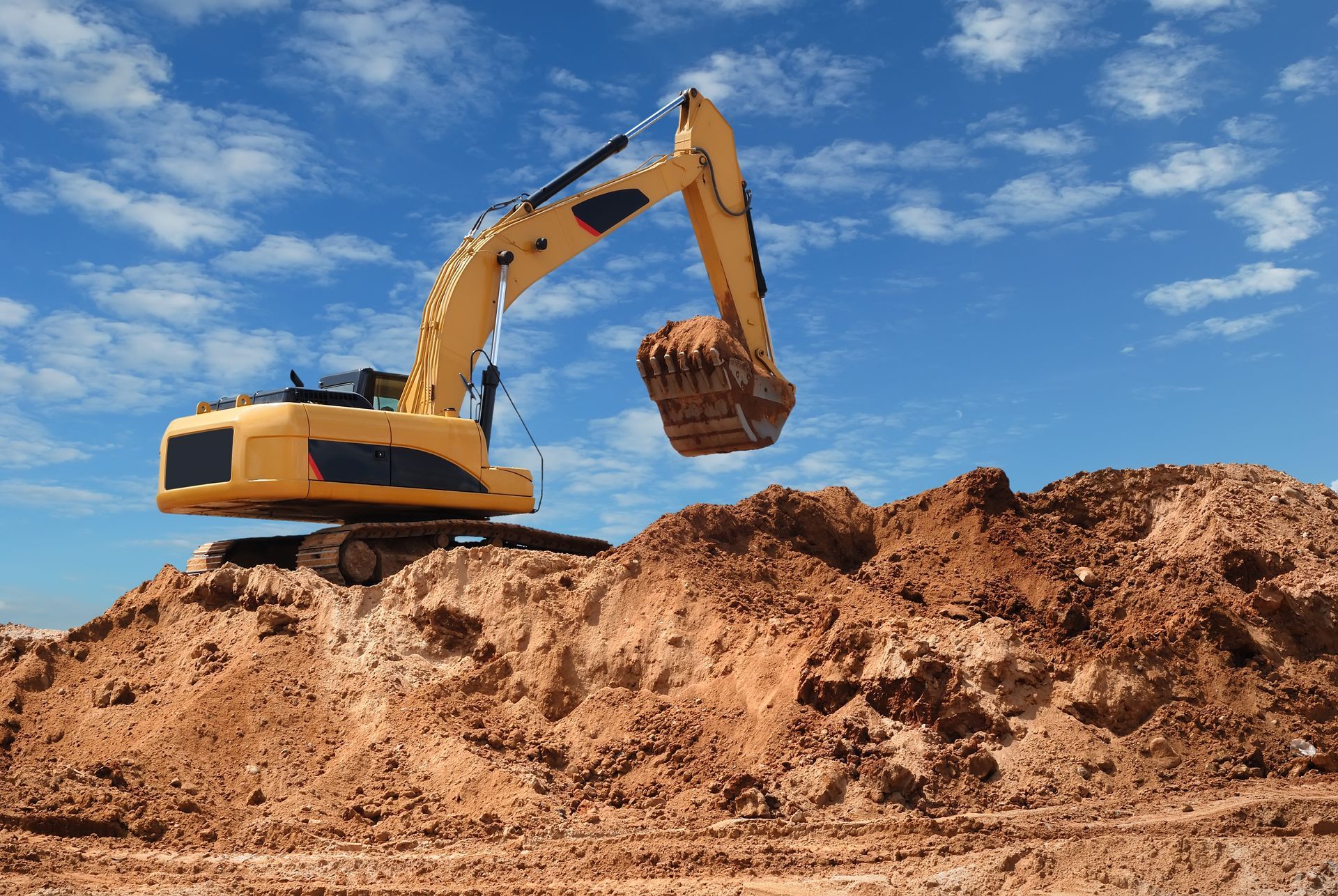 A yellow excavator is digging in a pile of dirt.