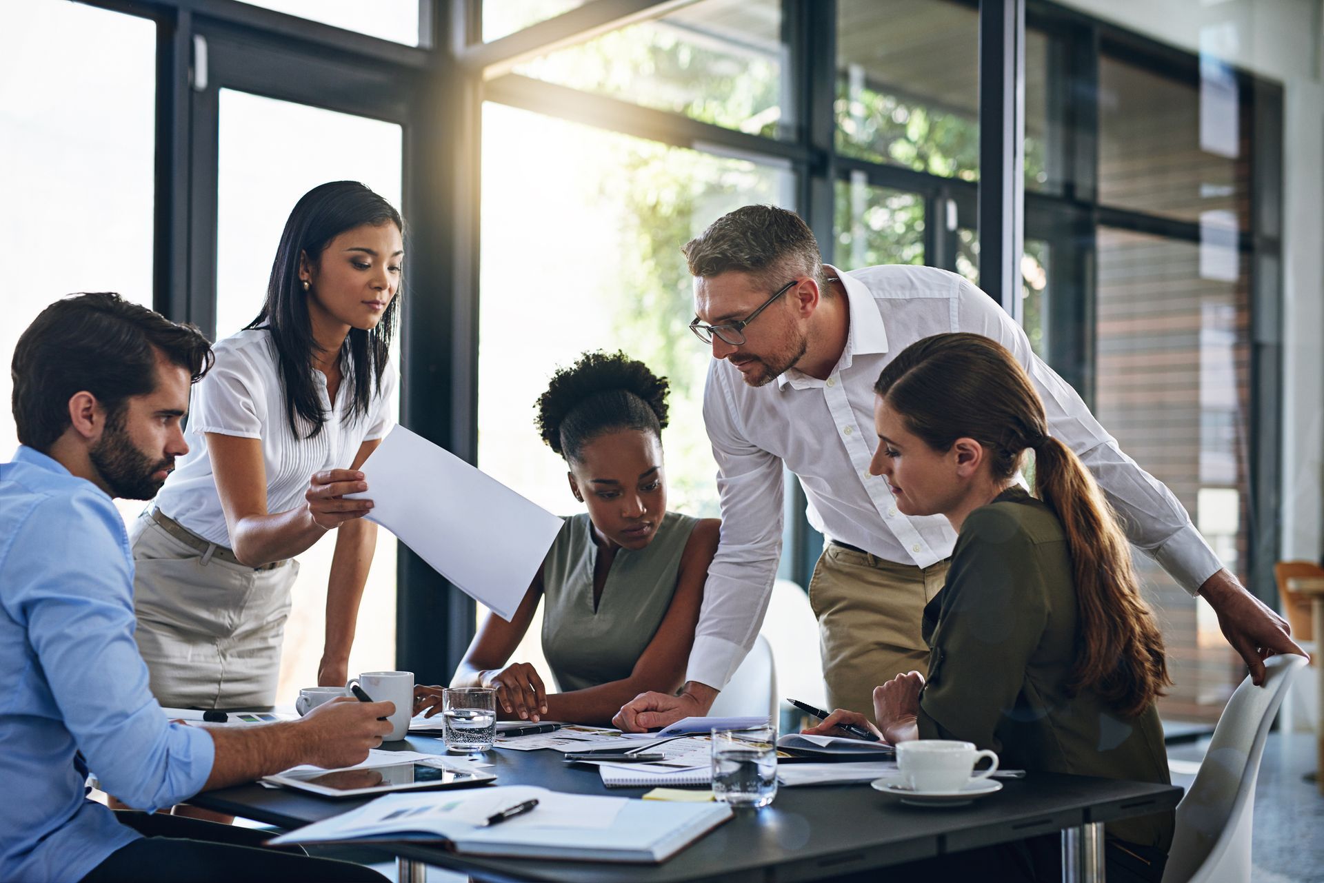 Group of diverse professionals collaborating around a table, reviewing documents and discussing ideas in a modern office.