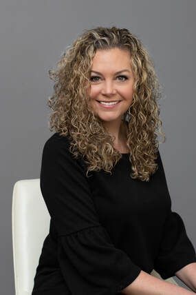 A woman with curly hair is sitting in a chair and smiling.