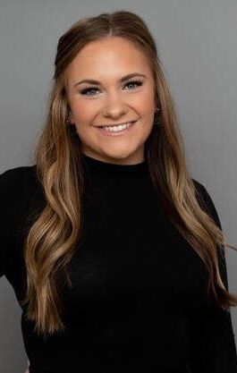 The woman is wearing a black turtleneck and smiling for the camera.