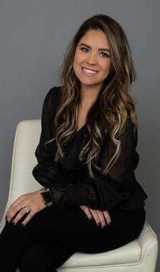 A woman is sitting in a chair with her legs crossed and smiling.