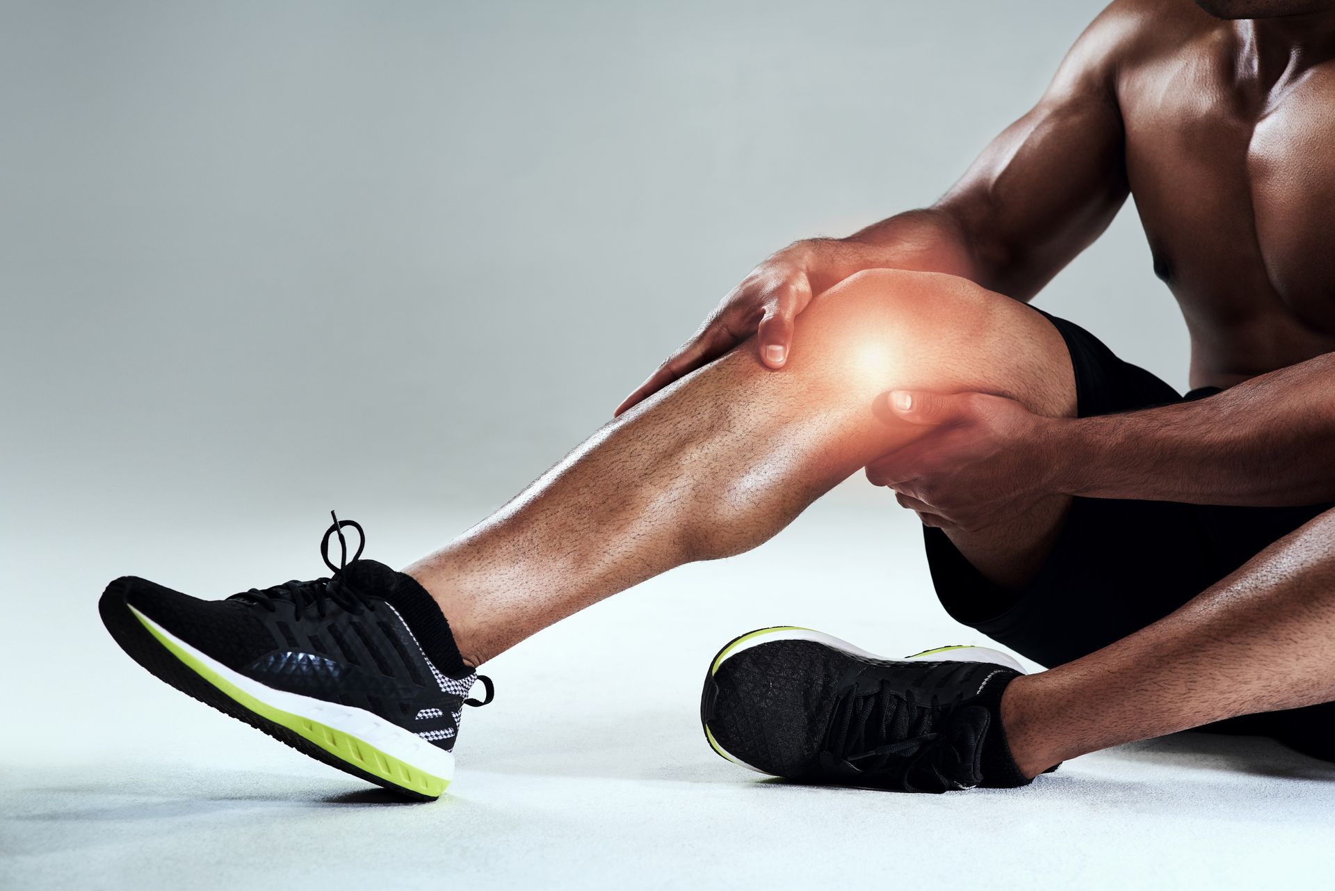A fit man sitting and holding his painful knee, highlighted with a glowing effect.