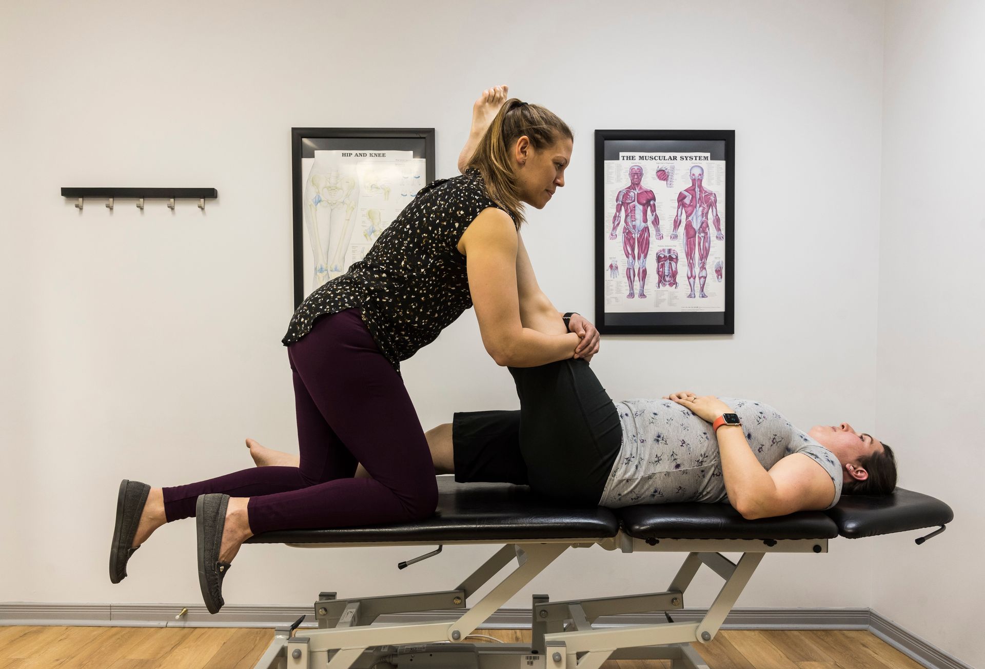 A woman is stretching a man 's leg on a table.