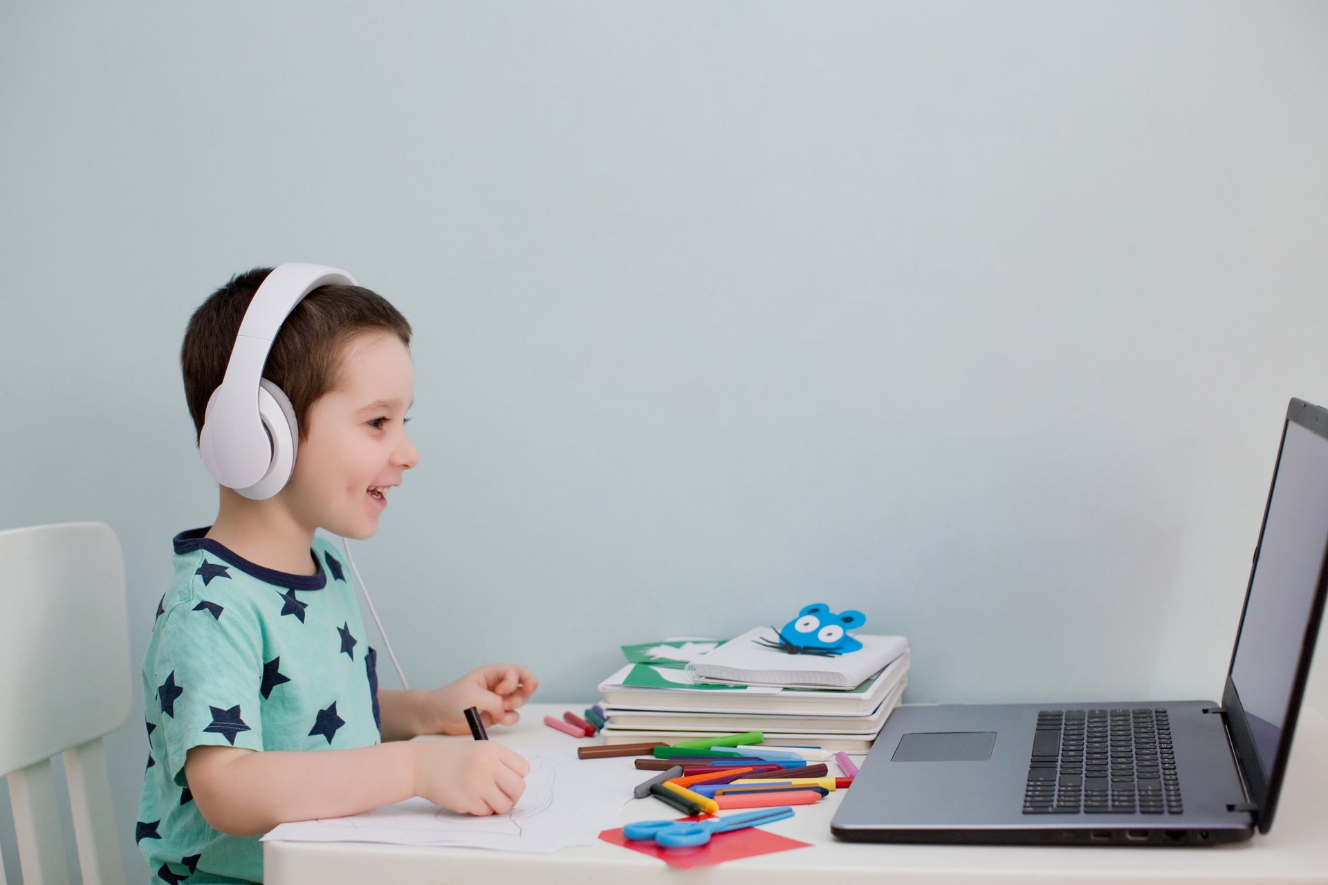 A young boy wearing headphones is sitting at a desk in front of a laptop computer.
