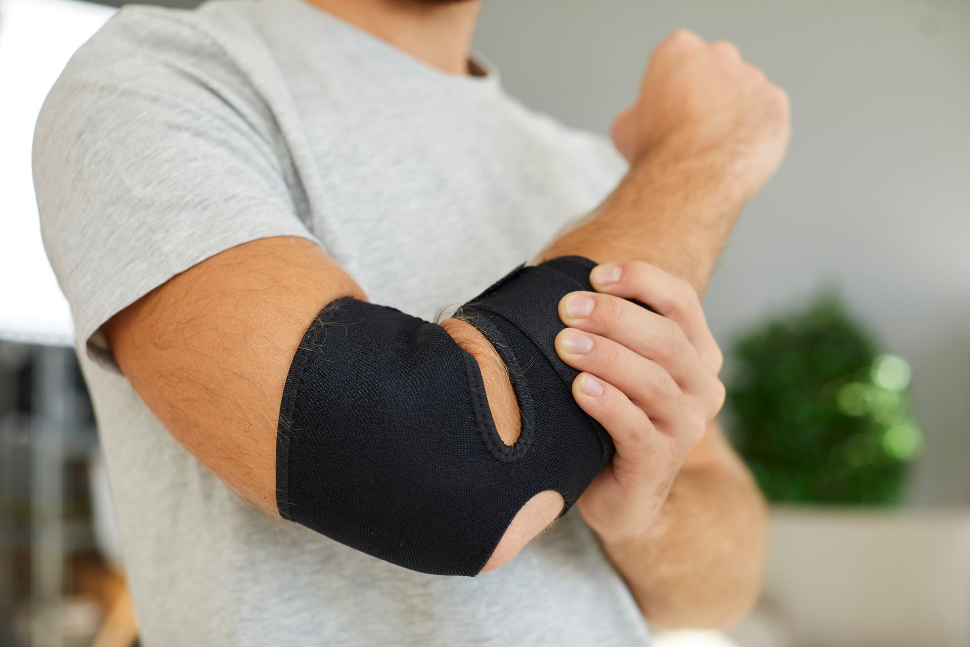 Person wearing a black elbow brace, holding wrist, indoors.