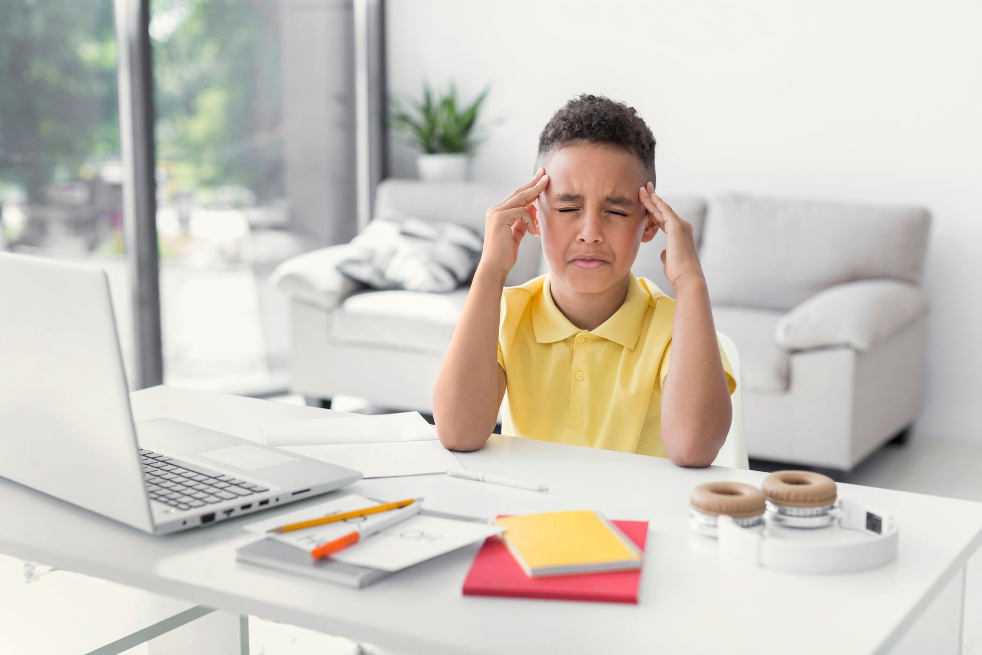 A young boy is sitting at a desk with his hands on his head.