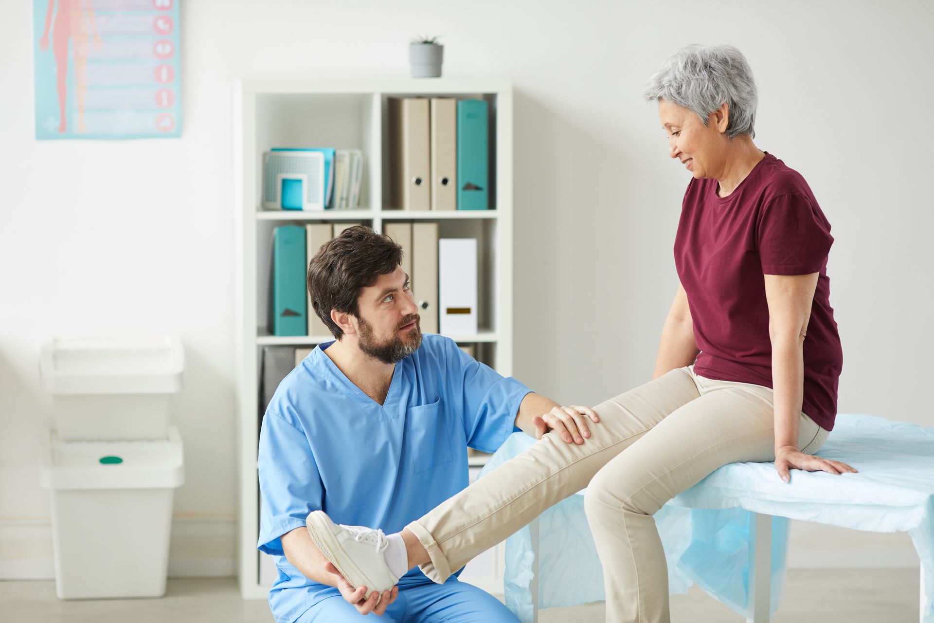 A healthcare professional examining an older woman's leg in a medical office.
