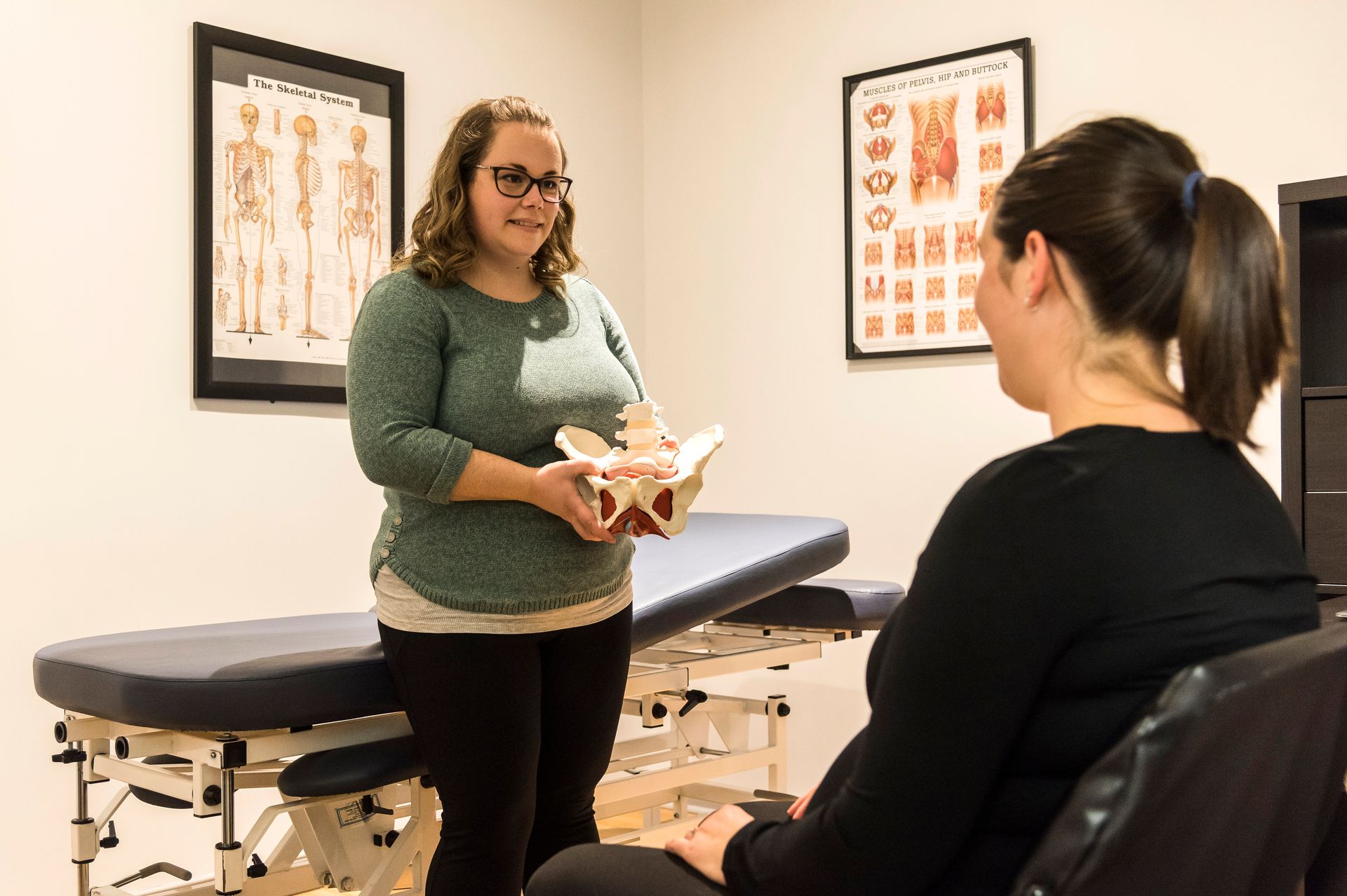 A woman is holding a model of a pelvis while talking to a pregnant woman.