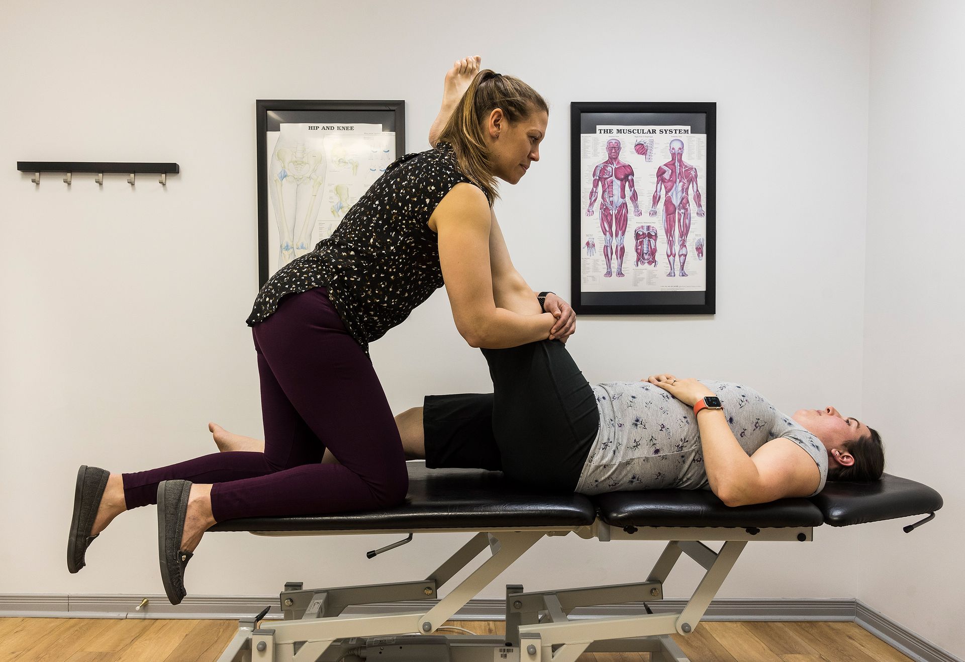 A woman is stretching a man 's leg on a table.