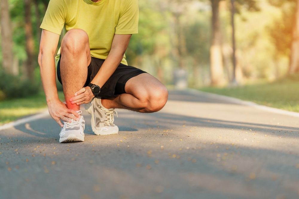 A man is kneeling down on the side of the road tying his shoelaces.