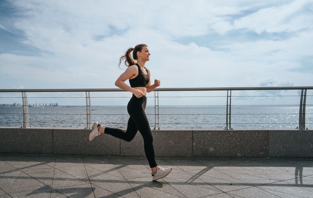 A woman is running on a sidewalk next to the ocean.