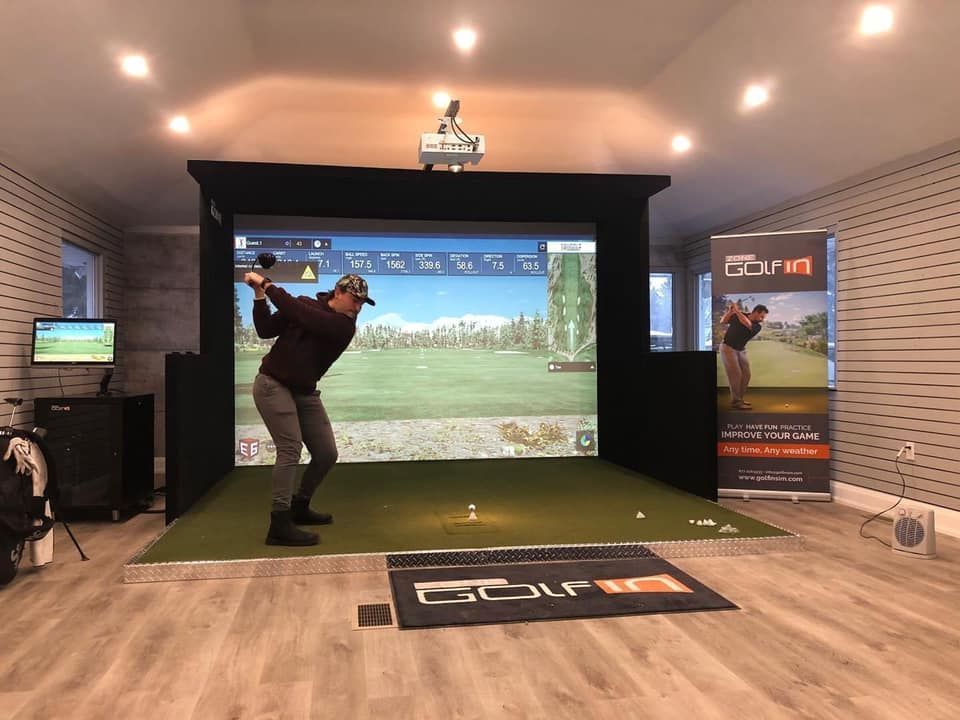A man is swinging a golf club in a golf simulator.