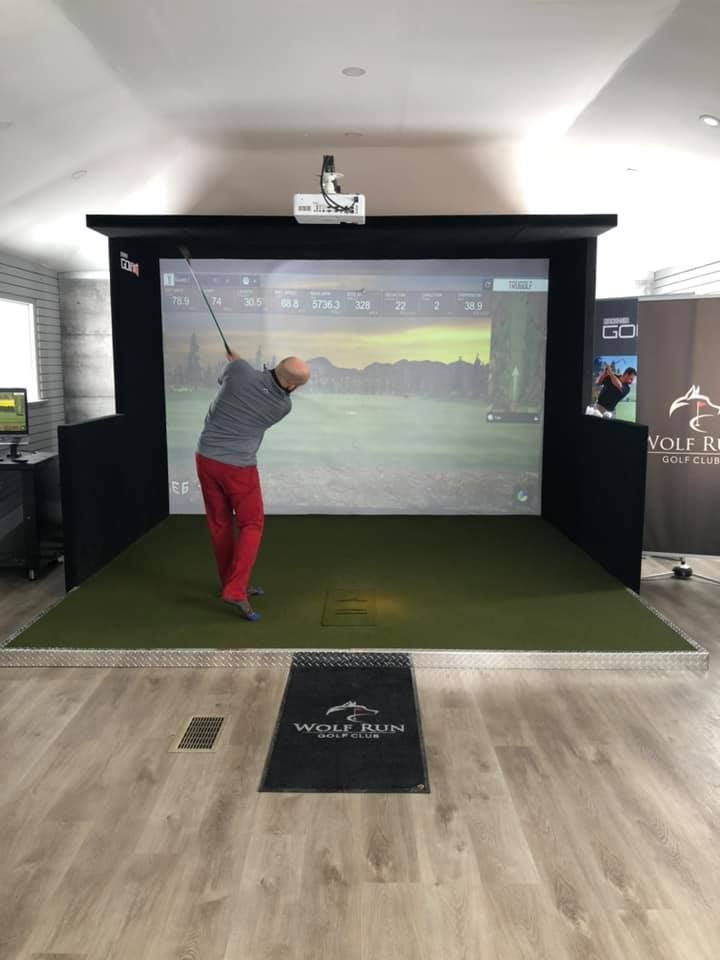 A man is swinging a golf club in a golf simulator.