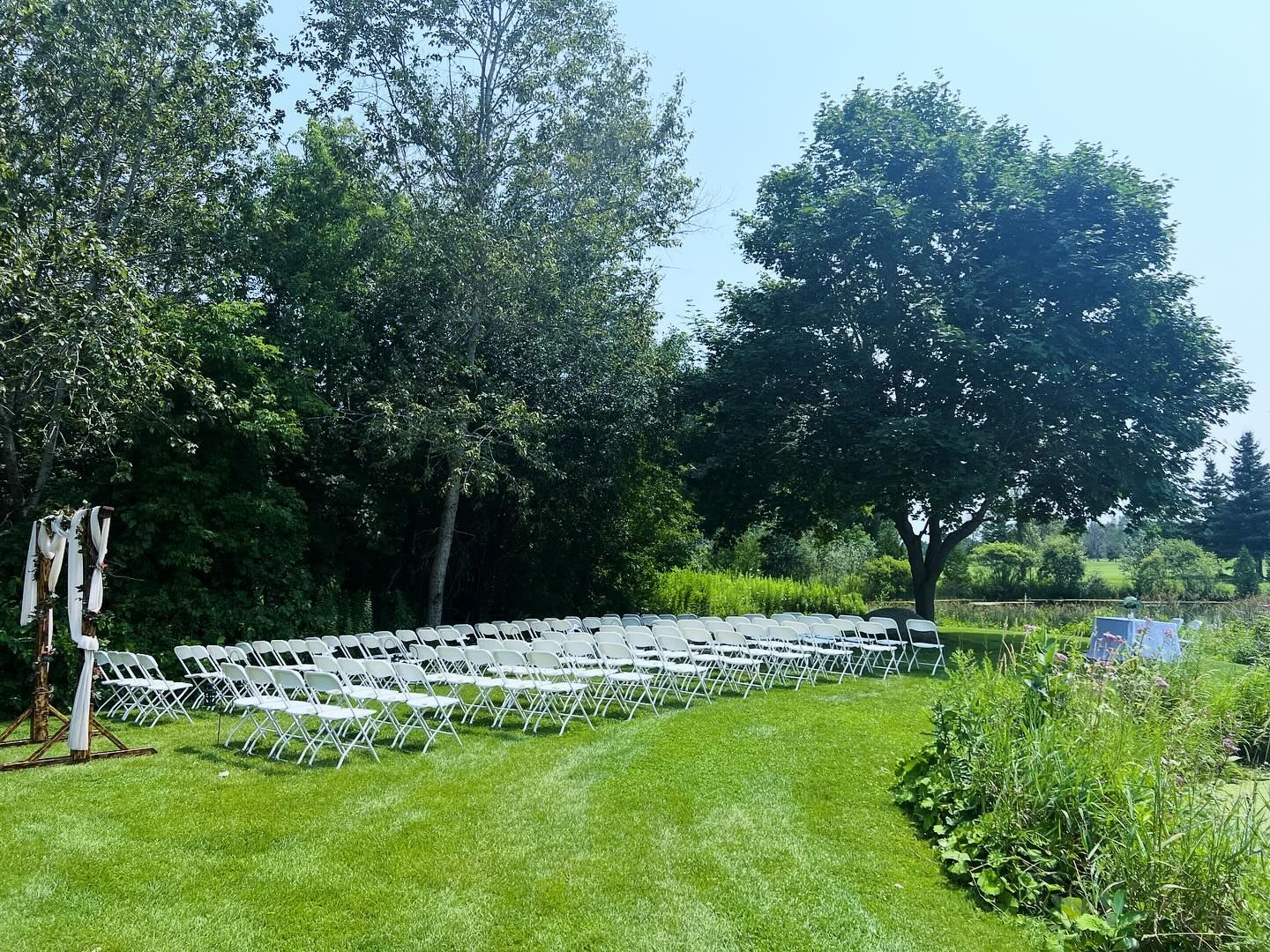 A row of white chairs are lined up in a grassy field.