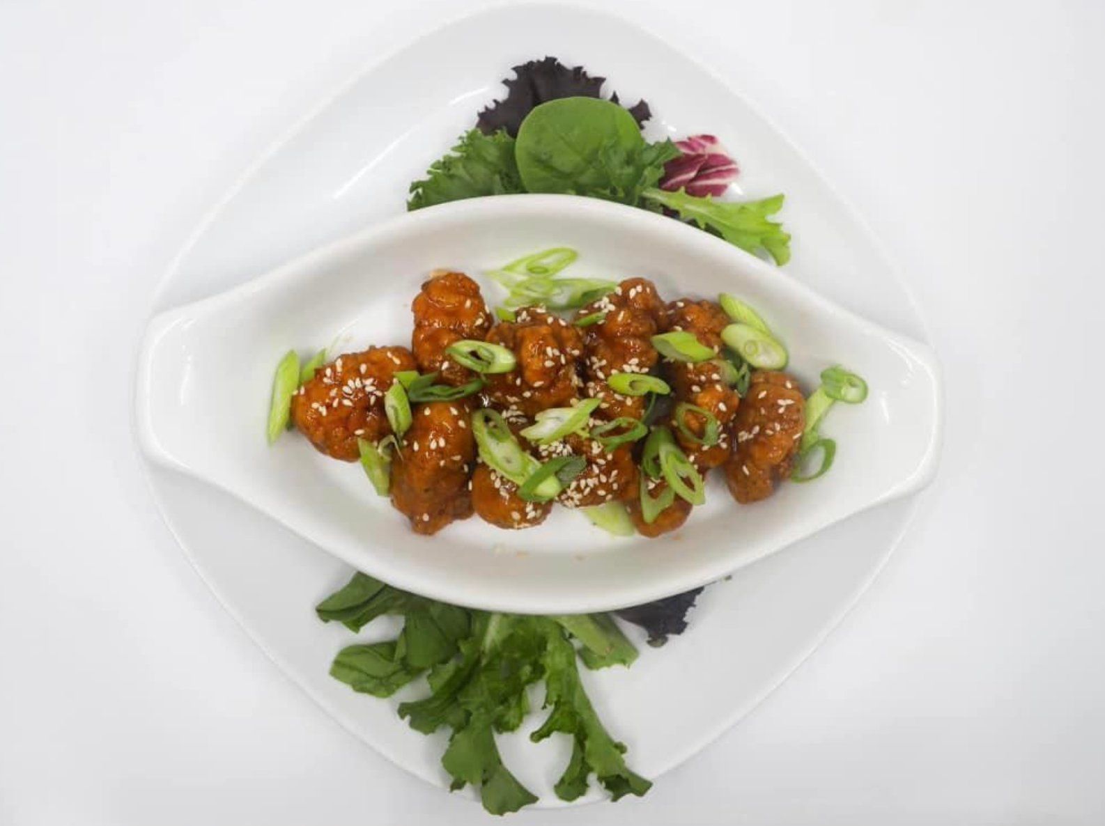 A white plate topped with a bowl of food and green onions.