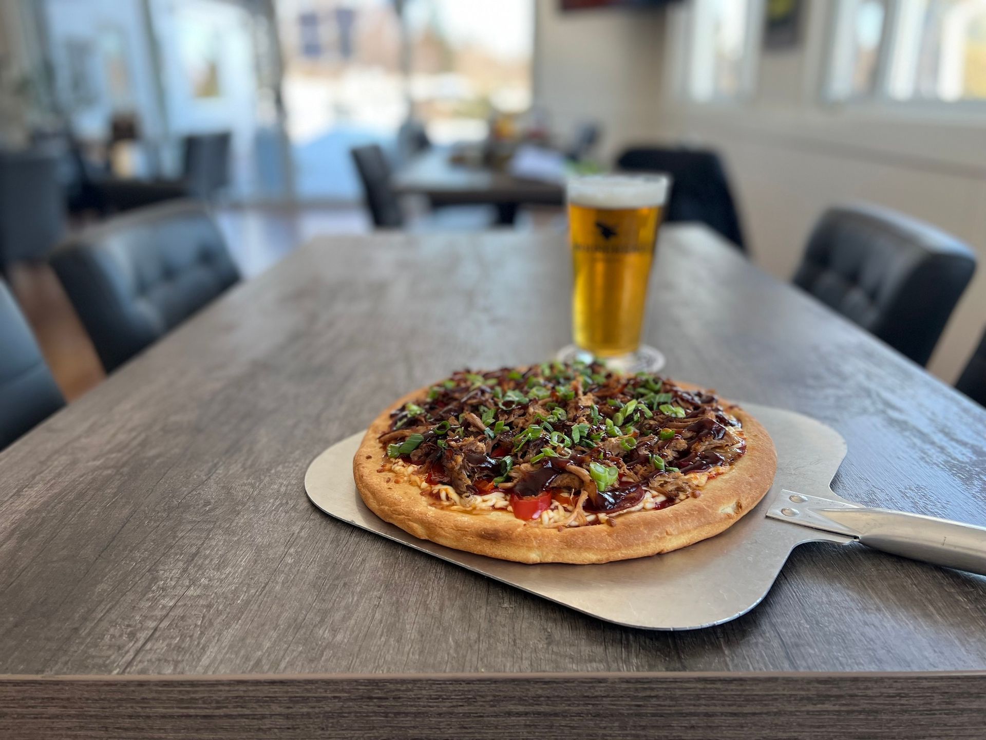 A pizza is sitting on a pizza pan on a table next to a glass of beer.