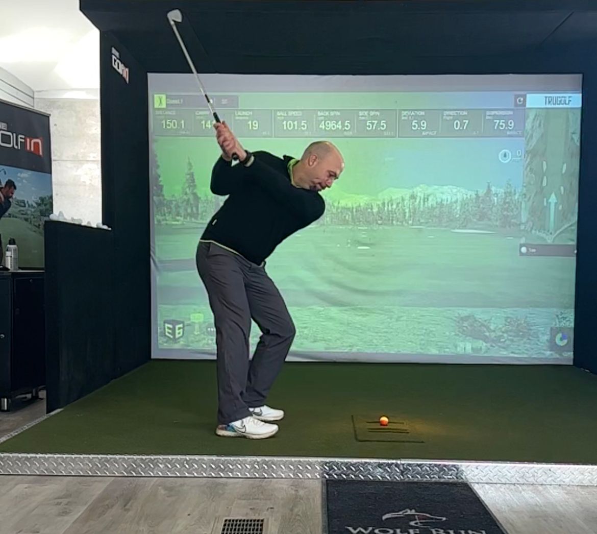 A man is swinging a golf club in front of a large screen.