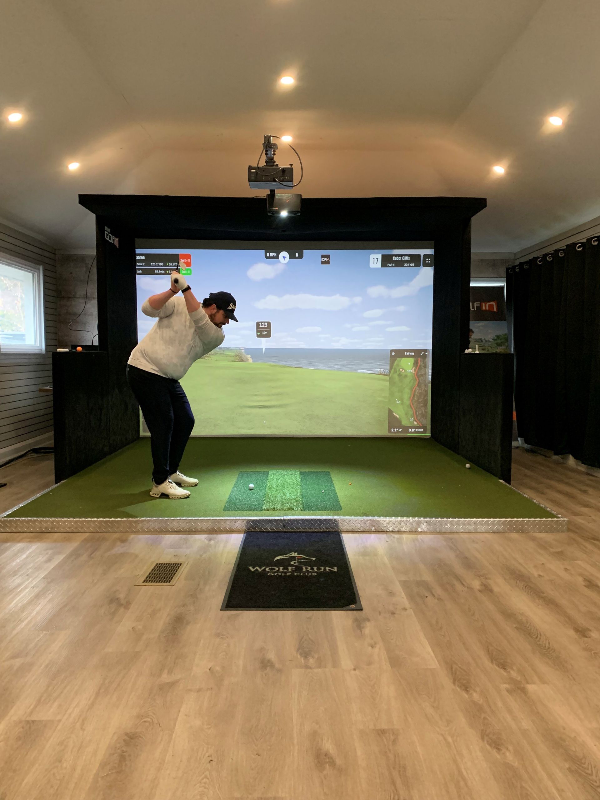 A man is swinging a golf club in front of a large screen.