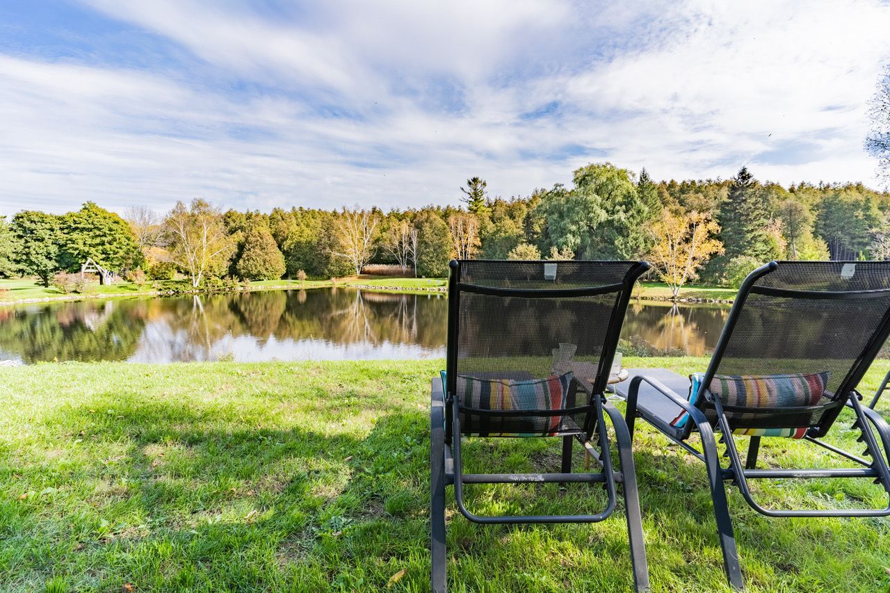 Two lounge chairs are sitting in the grass near a lake.