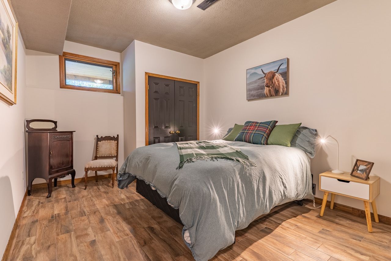 A bedroom with a bed , nightstand , chair and painting on the wall.
