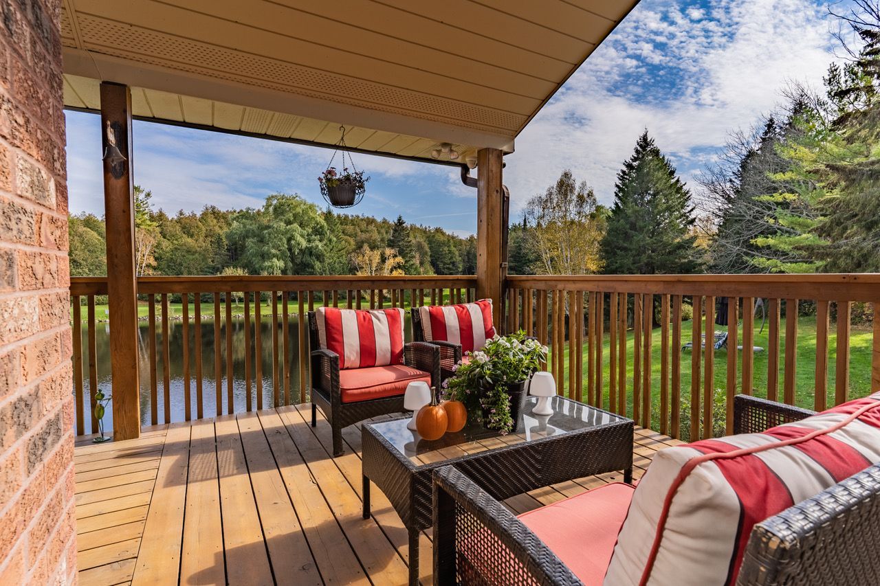A deck with a couch , chairs and a table overlooking a lake.