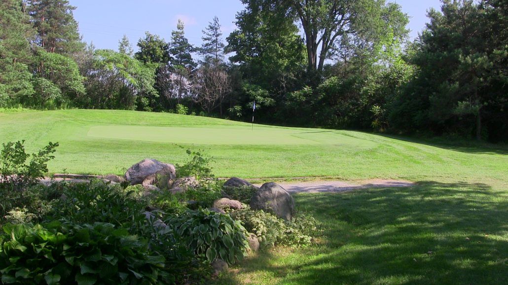 A golf course with a green and trees in the background.
