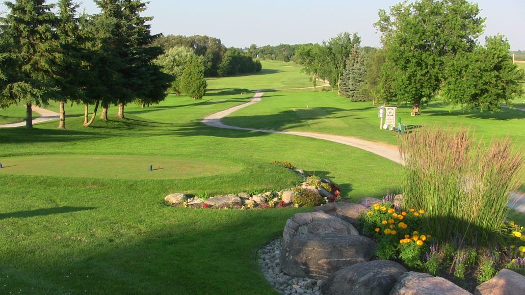 A view of a golf course with trees and rocks in the foreground.