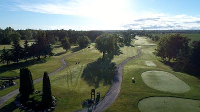 An aerial view of a golf course surrounded by trees on a sunny day.