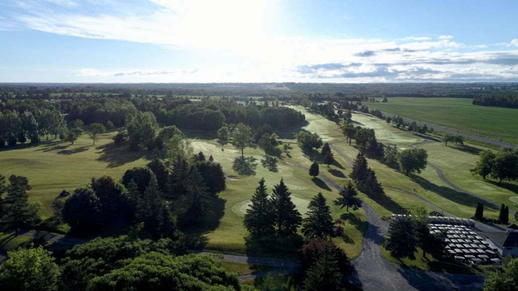 An aerial view of a golf course surrounded by trees on a sunny day.