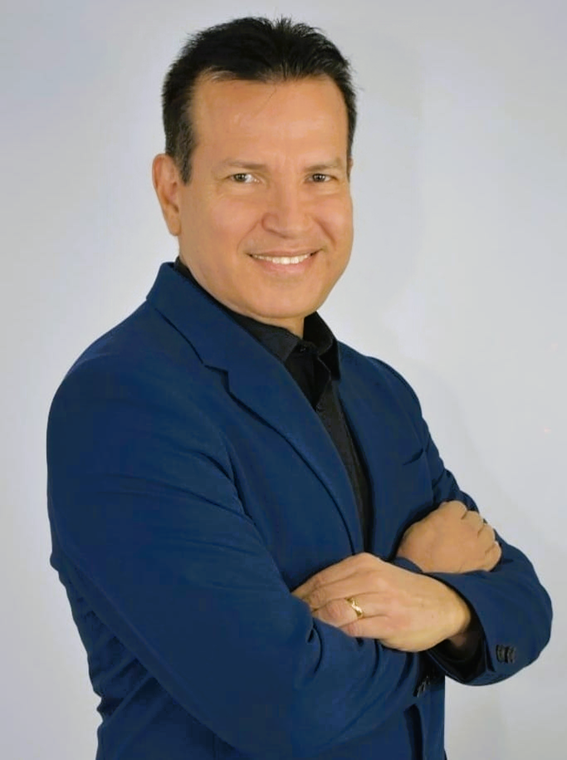 A man in a blue suit is smiling with his arms crossed