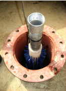 A well with a metal pipe and blue-bristled brush inside, set in a circular flange.