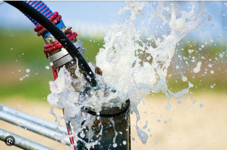 Water spraying from a black pipe with attached hoses, outdoors.