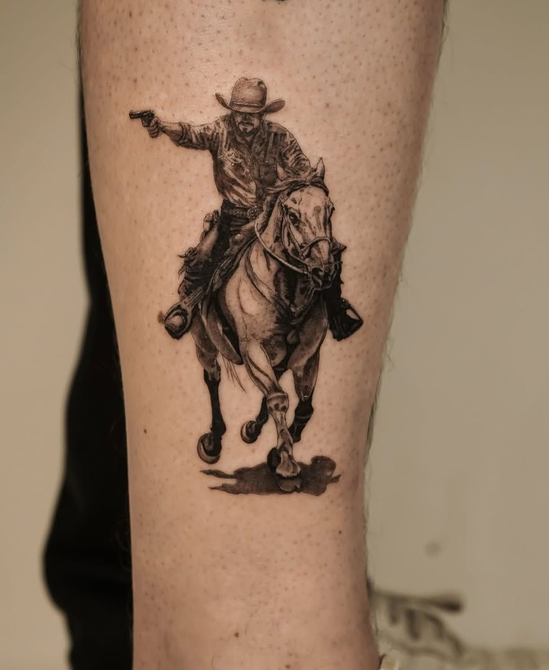 A black-and-grey tattoo on skin depicting a cowboy on a galloping horse, aiming a pistol to the side.