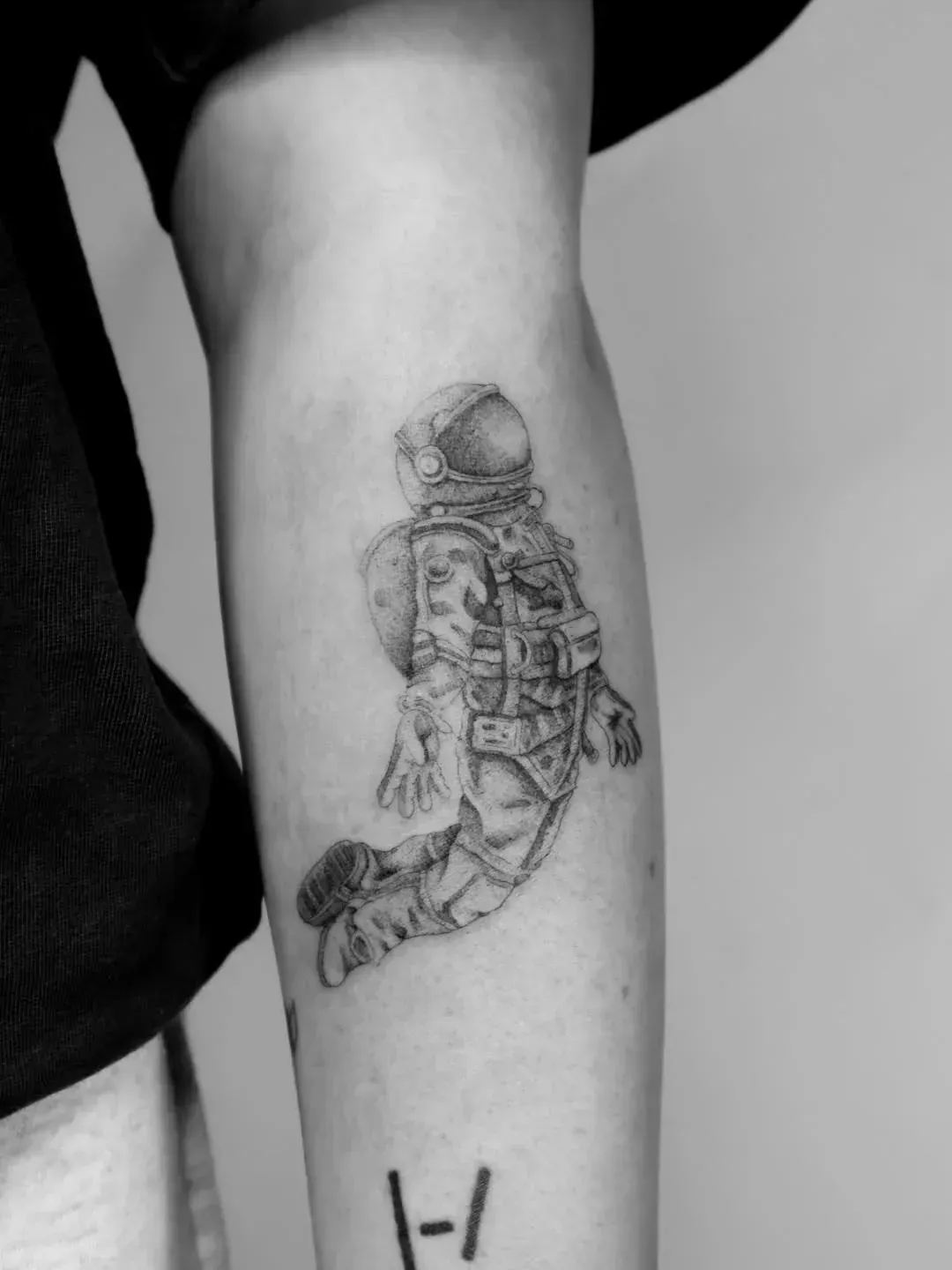 A black and white tattoo of an astronaut floating on a person's forearm, with a small Twenty One Pilots logo below.
