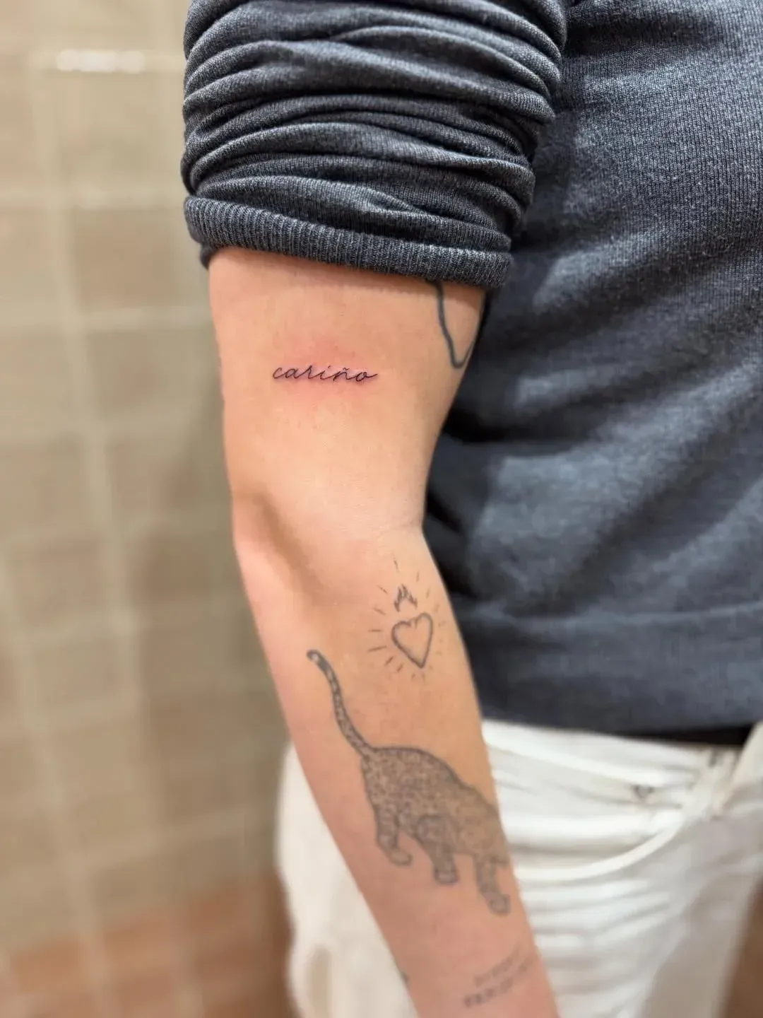 A person's arm features multiple small tattoos: the word 