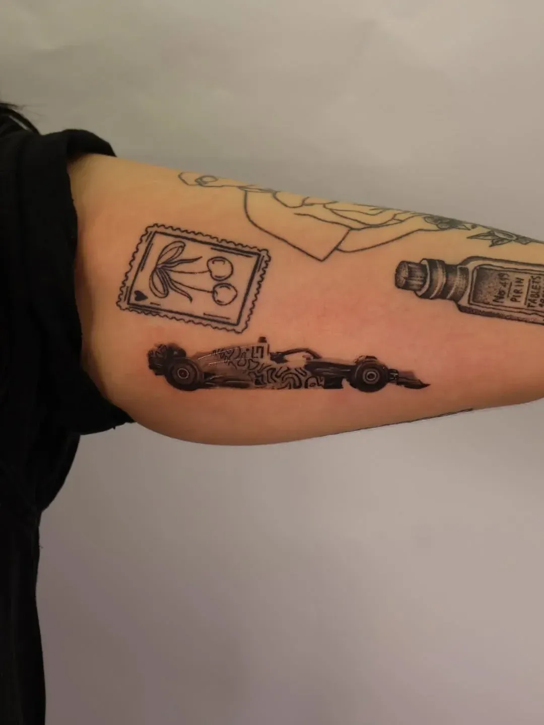 A black-ink tattoo of a Formula 1 race car on a person's upper arm, near other line-art tattoos.