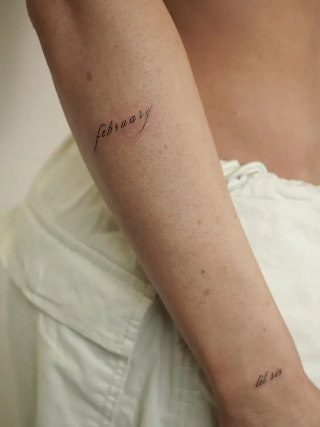 A close-up view of an arm featuring two small, fine-line script tattoos: 