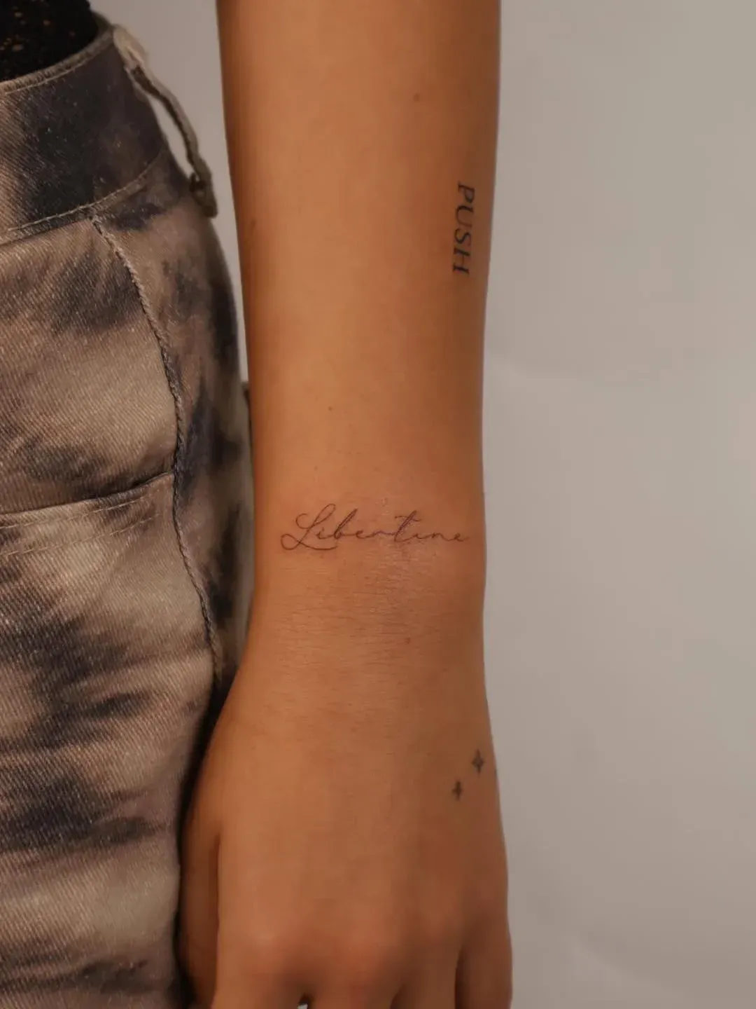 A person's forearm featuring two delicate script tattoos, with the word 