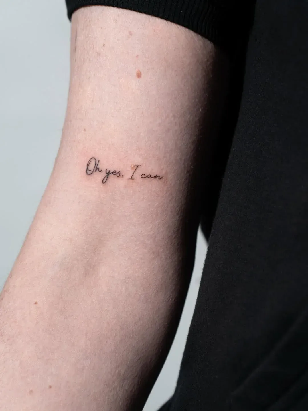 A close-up of an inner forearm with a minimalist, black cursive tattoo that reads: 