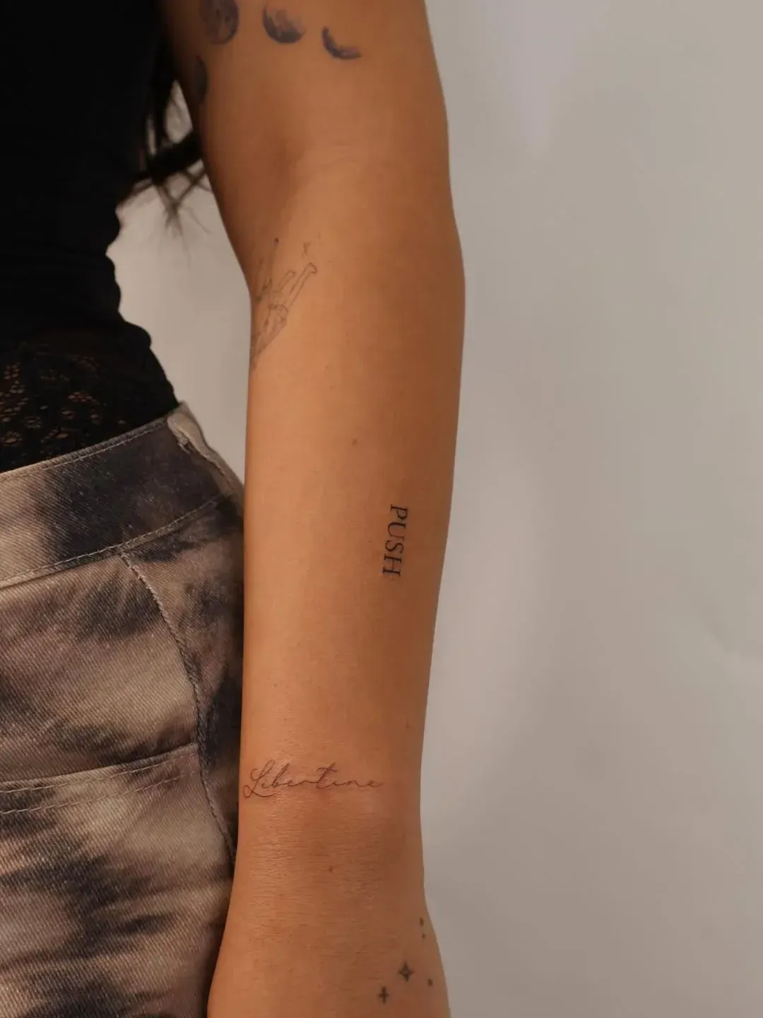 A person’s forearm with two tattoos: a small, serif-font 