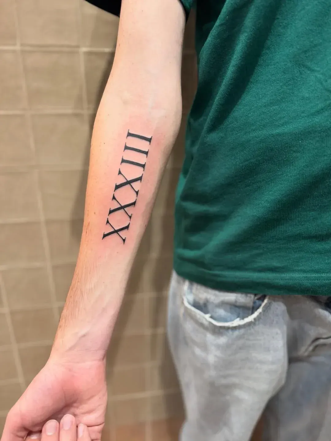A person's forearm featuring a tattoo of the Roman numeral XXXIII, written in a bold, black serif font.