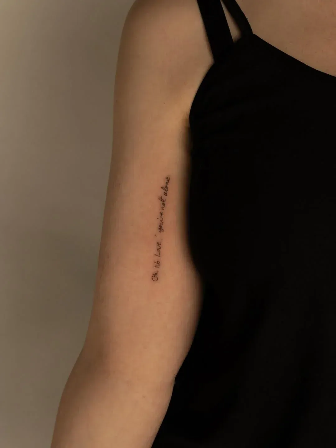 A person’s arm wearing a black top with a small, delicate vertical line tattoo of Arabic calligraphy.